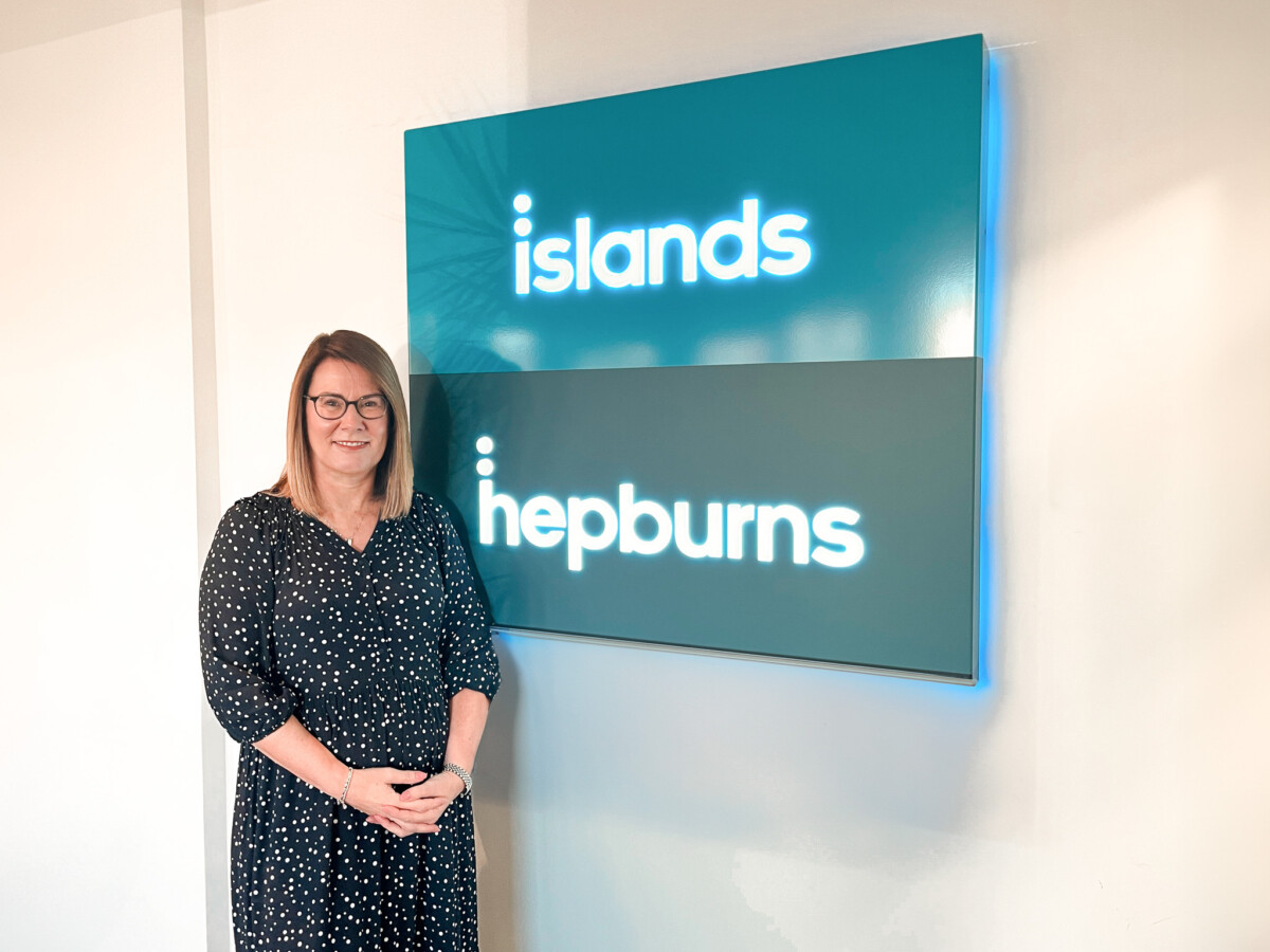 Shirley Lester, newly appointed Board of Directors member at Islands Insurance Group, standing in front of the Islands and Hepburns logo.